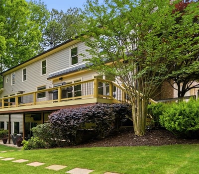 Discover a spacious home with a large deck, surrounded by lush landscaping and vibrant greenery.
