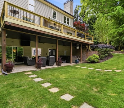 Spacious outdoor living area features a deck overlooking a lush, landscaped yard with stone pathways.