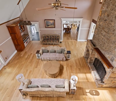 Spacious living area with vaulted ceilings, a rustic stone fireplace, and abundant natural light throughout.
