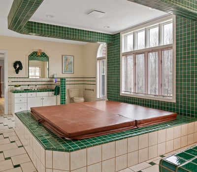 This unique bathroom features a sunken hot tub surrounded by vibrant green tile accents and ample natural light.