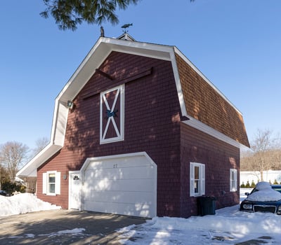 Unique barn-style home with ample space and convenient garage, set in a picturesque winter landscape.