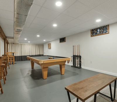 Spacious recreational room featuring a billiards table, bar seating, and ample natural light from large windows.