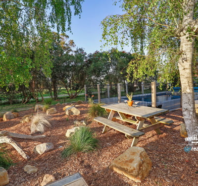 This outdoor space features a picnic area surrounded by native landscaping and a pool in the background.