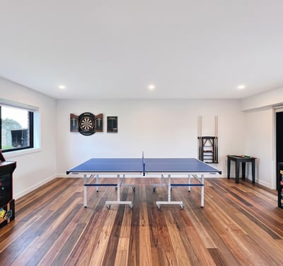 Bright recreational space featuring a ping pong table, arcade machine, and dartboard for entertainment.