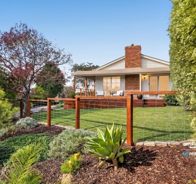 This inviting home features a spacious yard surrounded by vibrant landscaping and a welcoming front porch.