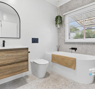 Modern bathroom featuring a freestanding tub, large mirror, and ample natural light from the window.