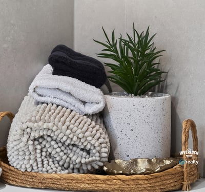 This inviting bathroom features neatly arranged towels and a contemporary plant in a chic basket.
