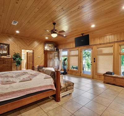 Spacious master bedroom featuring wood accents, large windows, and direct access to outdoor greenery.