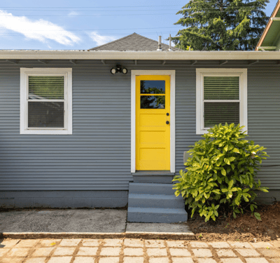 Bright and inviting home featuring a distinctive yellow door, ample natural light, and a spacious front yard.