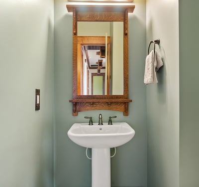 Designer half bath with pedestal sink, custom mirror, and handcrafted wood accents. A polished space that adds charm and convenience for visitors.
