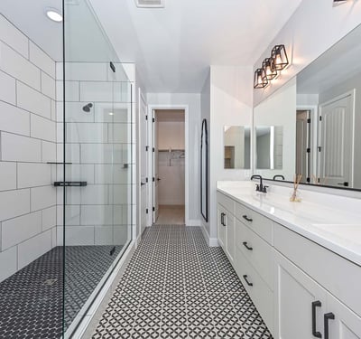 A luxurious retreat featuring geometric tile floors, walk-in glass shower, dual sinks, and upgraded matte black fixtures.