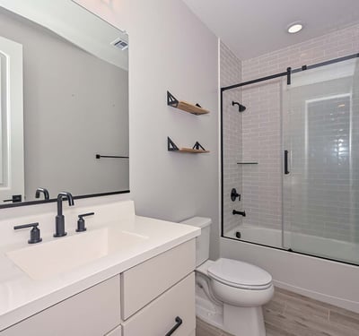This modern hall bathroom showcases a tiled tub/shower combo, black framed glass doors, and a crisp white vanity for a polished look.
