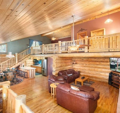Bright great room with vaulted ceilings, hardwood floors, and exposed log beams. The open layout offers flexible living and entertaining space.