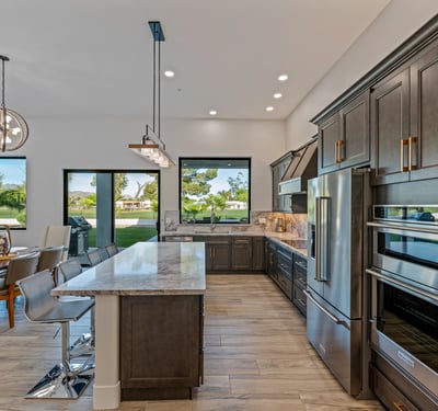 A chef s kitchen with premium appliances, marble counters, and a large island overlooks backyard and golf course views.