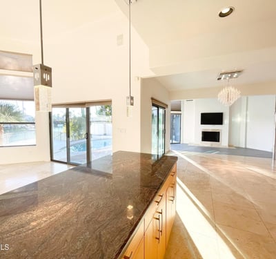Gourmet kitchen with open flow into living area. Refined pendant fixtures and granite surfaces define this bright, upscale space.