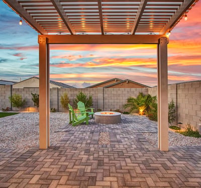 The fire pit area shines under sunset skies, surrounded by Adirondack chairs, desert plants, and durable pavers. A great space for evening gatherings in Litchfield Park.