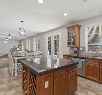Bright kitchen with wood cabinetry, granite island, tile flooring, and large windows bringing in natural light from the backyard.