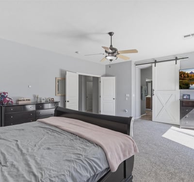 Elegant primary bedroom with barn-style sliding door access to the bathroom, spacious layout, and soft carpeting for a comfortable and stylish retreat.