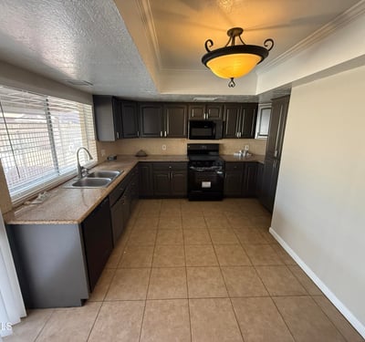 Glendale kitchen with dark cabinetry, tile floors, and ample prep space. Large window above the sink provides natural light and views toward the backyard pool area.