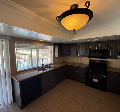 Well-designed kitchen featuring dark cabinets, tile flooring, and practical layout. The sink window overlooks the fenced backyard and pool, bringing outdoor views into the space.