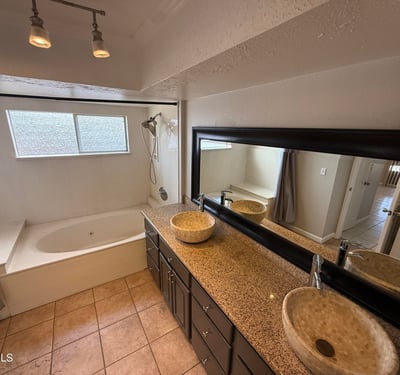 Primary bathroom featuring granite countertops, dual vessel sinks, and large mirror for added functionality. Tile flooring and warm finishes create a comfortable and practical bathroom space.