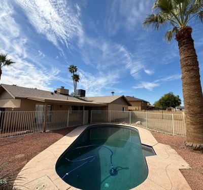 Private backyard featuring a Pebble Tec pool framed by mature palm trees and block wall fencing. The tranquil outdoor setting enhances the home s relaxing backyard atmosphere.