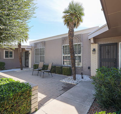 Private courtyard patio with pavers, mature landscaping, and seating area ideal for outdoor entertaining or enjoying quiet mornings in Sun City.