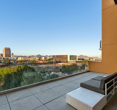 Spacious balcony with modern seating and glass railing, offering beautiful city and park views in Phoenix.
