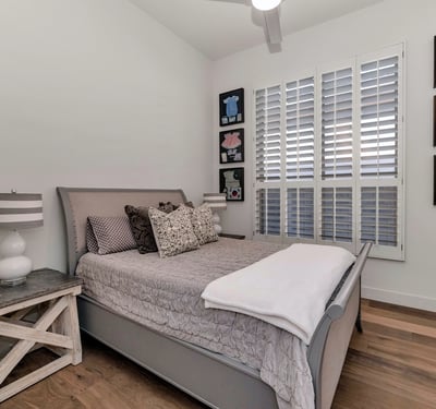 Bright guest bedroom with plantation shutters, wood floors, and neutral finishes, offering a relaxing space in this Phoenix home.