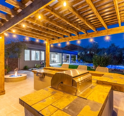 Scottsdale pergola kitchen with built-in grill, bar seating, and warm lighting, ideal for entertaining after sunset.