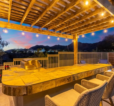 Scottsdale backyard featuring a pergola-covered bar with seating and string lights, perfect for entertaining guests.