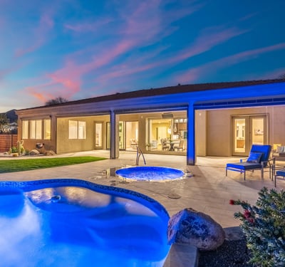 Scottsdale backyard featuring glowing spa, poolside seating, and covered patio, ideal for evening relaxation and entertaining.