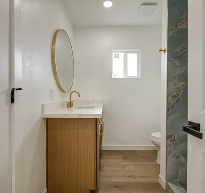Featuring a quartz vanity, stylish round mirror, modern fixtures, and a beautifully tiled shower, this renovated bathroom combines comfort with contemporary design.