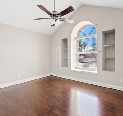 Soaring vaulted ceilings, decorative wall niches, wood flooring, and an elegant arched window create a bright and welcoming bedroom filled with natural light.