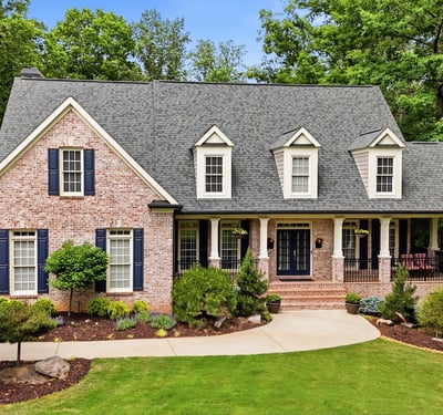 Beautiful brick home nestled in nature, featuring a spacious porch and well-maintained landscaping in a peaceful setting.