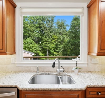 Bright kitchen featuring rich wood cabinetry and a scenic view of lush greenery through a large window.