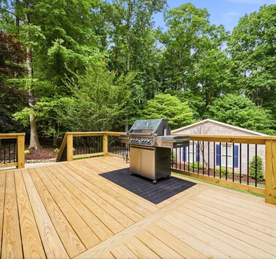 Spacious deck featuring a built-in grill, perfect for outdoor entertaining amid a lush, wooded backdrop.