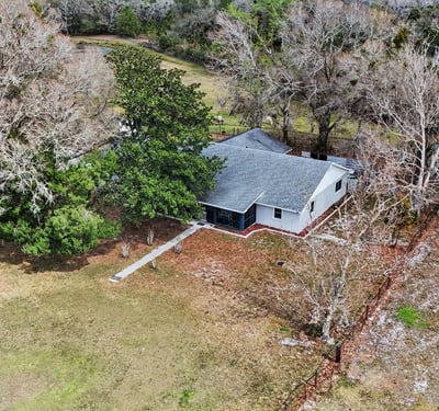 Aerial photo of the house with a front sidewalk as well as a rear entry sidewalk located off of the two car garage and paved slab parking area. This home is surrounded by mature trees and landscaping!