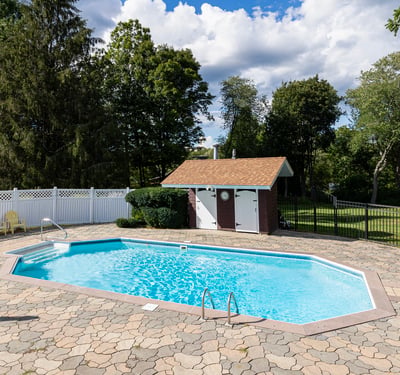 Inviting outdoor space features a spacious pool surrounded by lush greenery and a convenient shed for storage.