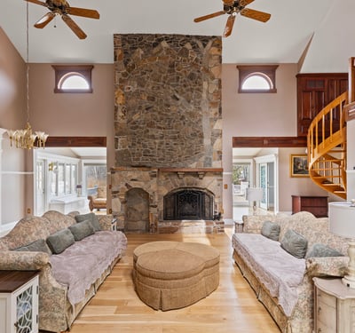 Spacious living area features a striking stone fireplace and unique spiral staircase, perfect for entertaining.