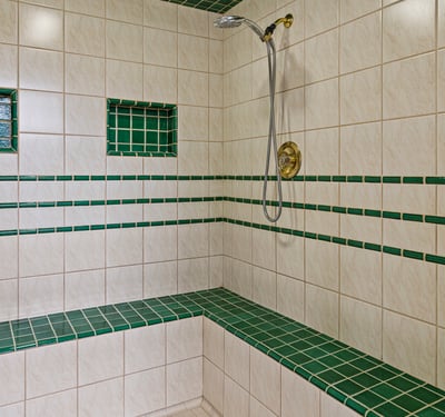 Spacious walk-in shower featuring unique green tile accents and built-in seating for added convenience.