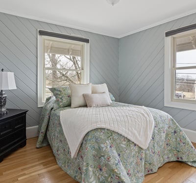 This inviting bedroom features cozy decor, ample natural light, and a tranquil view from the windows.