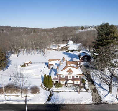 This expansive property features a beautiful home surrounded by lush trees and serene winter landscapes.