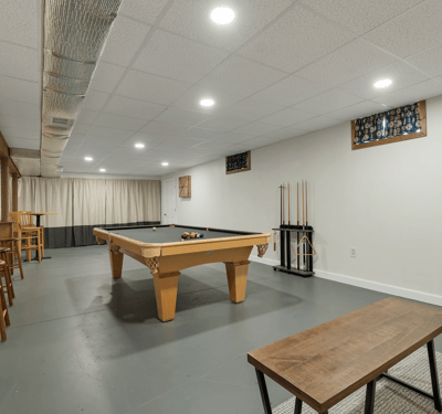 Spacious recreational room featuring a billiards table, bar seating, and ample natural light from large windows.