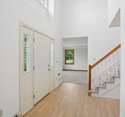 Bright and inviting entryway featuring a two-story ceiling, staircase, and views of the spacious living area.