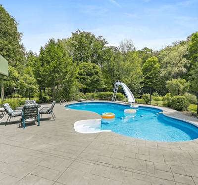 Enjoy summer days by the inviting pool featuring a slide, surrounded by lush greenery and relaxing loungers.