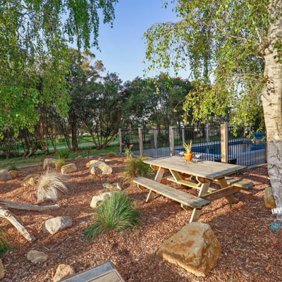 This outdoor space features a picnic area surrounded by native landscaping and a pool in the background.