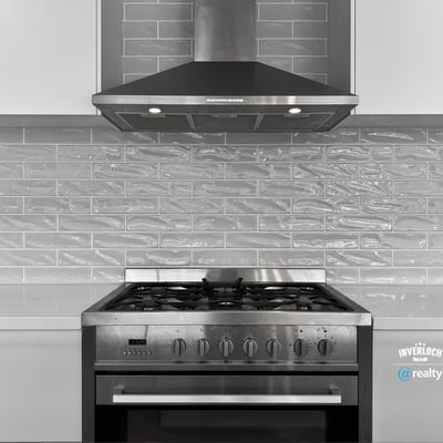 Modern kitchen featuring a stainless steel gas range and sleek gray tile backsplash for optimal cooking experience.