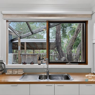 Bright kitchen featuring a large window that overlooks a spacious backyard with mature trees.