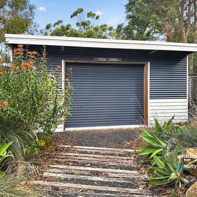 This functional tool shed offers practical storage solutions, surrounded by lush landscaping and natural beauty.